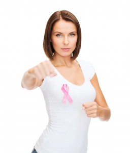 A woman with a pink breast cancer ribbon attached over one breast and punching forward