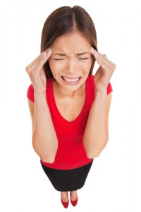 A woman in a red top and black skirt holding her hands to her temples in pain