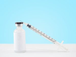 Needle syringe and jar of dermal filler on blue background.