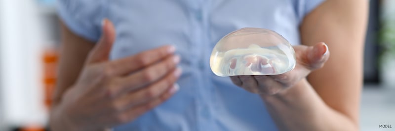 Woman in scrubs holding a breast implant.