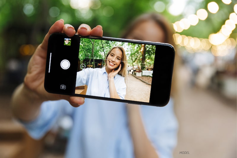 Woman taking selfie outdoors under tree cover