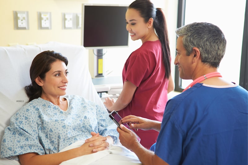 Smiling woman in hospital gown talking with doctor and nurse