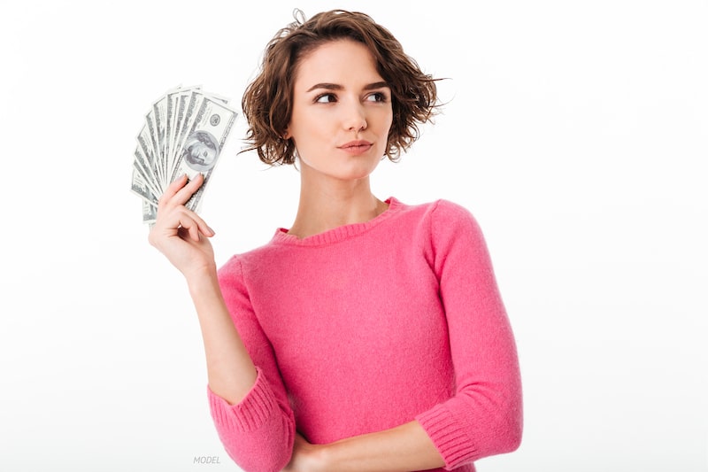 Woman holding a stack of cash, pondering something.