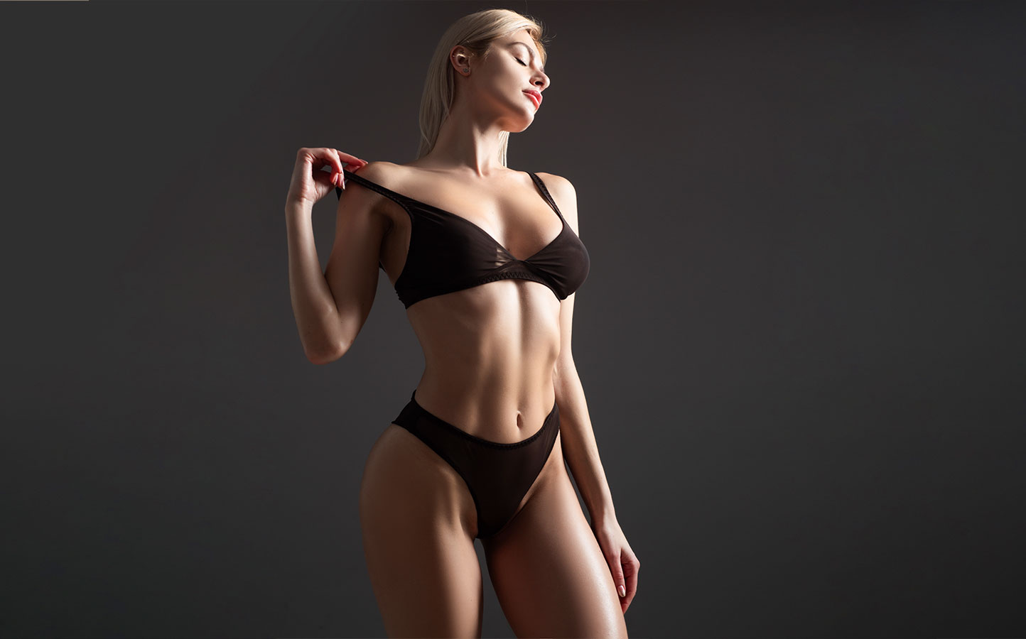Fit woman in black undergarments taking off bra strap