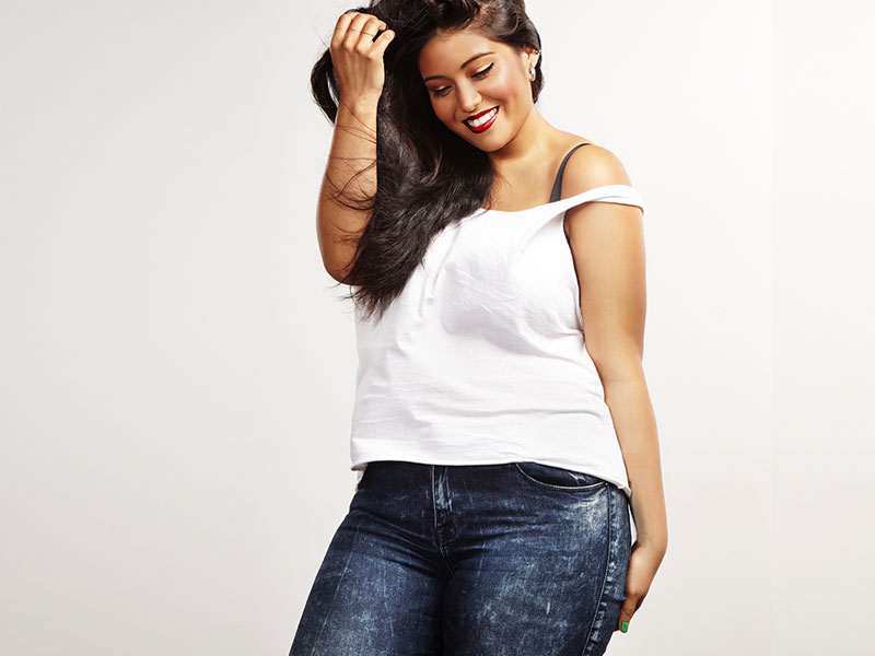 Curvy woman in jeans and a white shirt brushing her hair back
