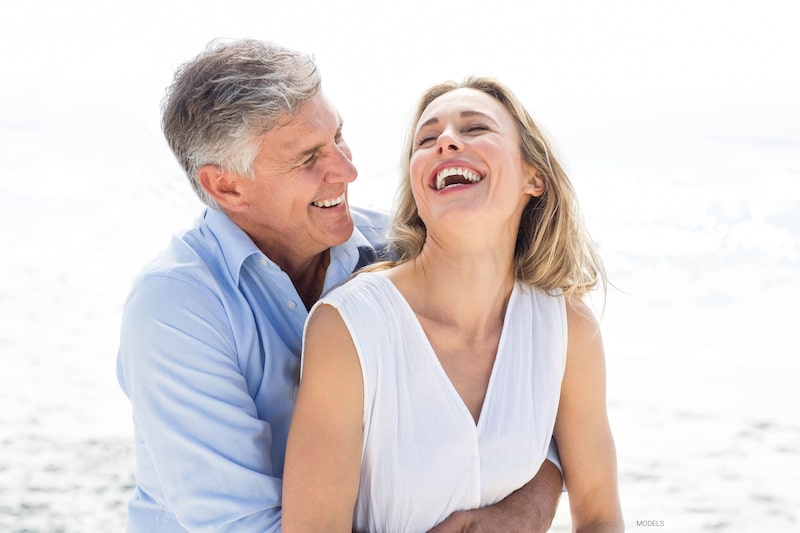Attractive older couple holding each other and laughing together on the beach