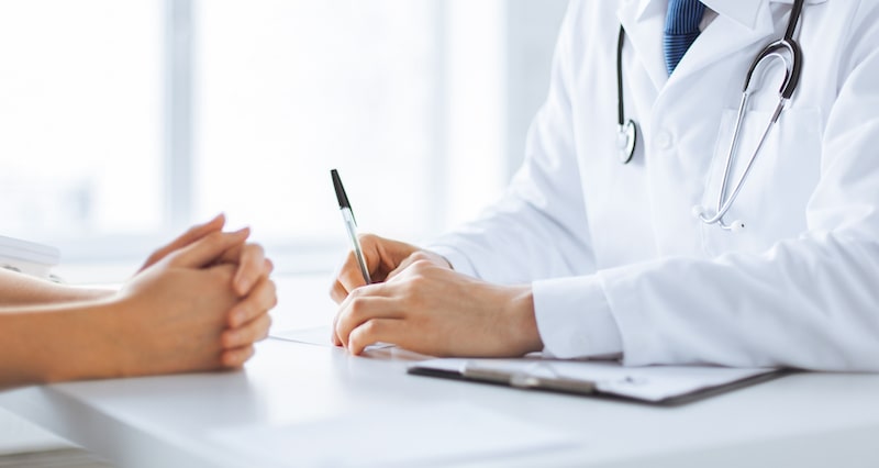 Close-up image of a woman's folded hands and a cosmetic surgeon during a consultation