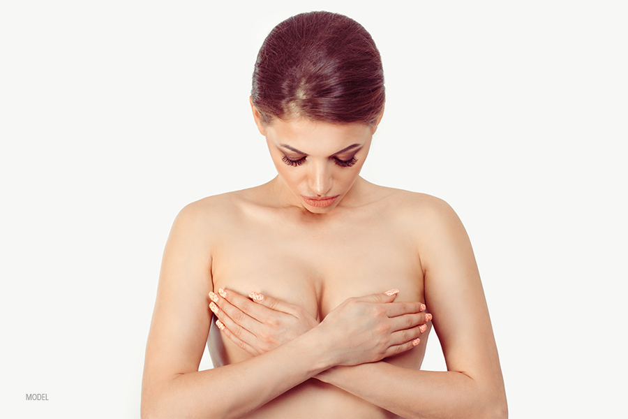 woman covering her breasts with her hands, looking down at her chest