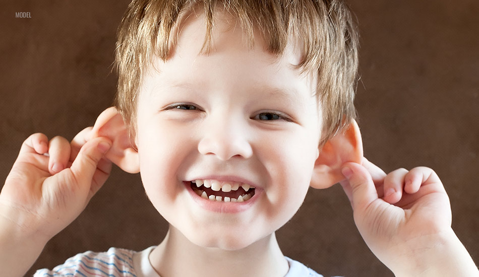 Happy little boy pulling his ears outward in a playful manner.